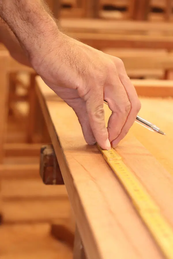 Hand reißt mit Zollstock und Bleistift ein Maß auf einem Brett an